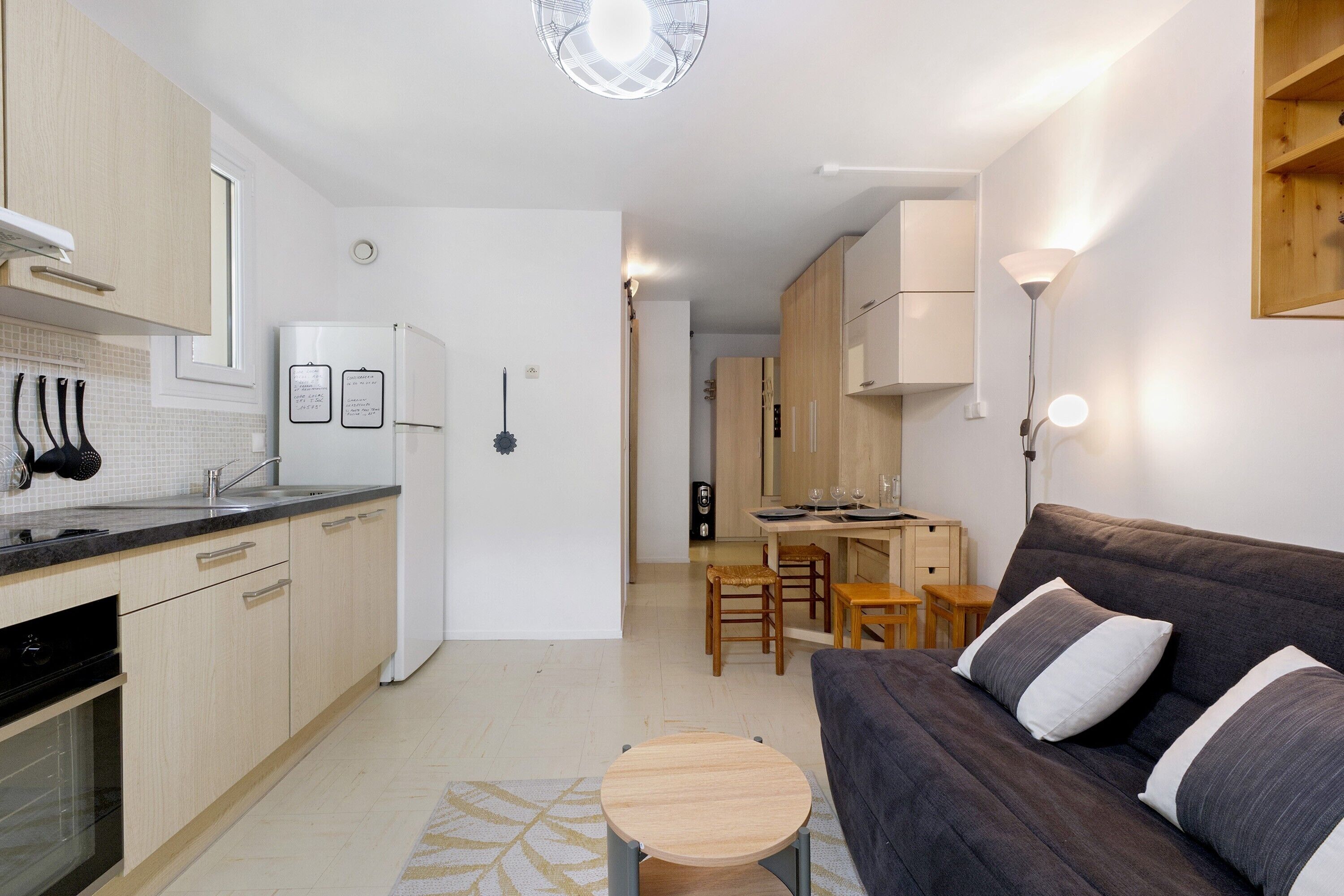 Une cuisine moderne équipée d’un réfrigérateur, d’une cuisinière et d’un évier. On y trouve également un coin repas avec une table et des chaises. Un canapé et une petite table ronde se trouvent dans l’espace salon.