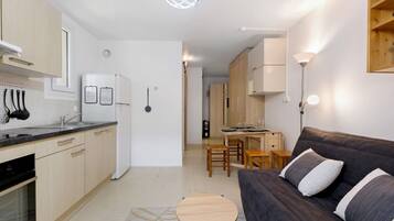 Une cuisine moderne équipée d’un réfrigérateur, d’une cuisinière et d’un évier. On y trouve également un coin repas avec une table et des chaises. Un canapé et une petite table ronde se trouvent dans l’espace salon.