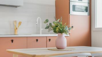 Een keuken met een houten tafel, een roze vaas met bloemen en een witte gootsteen.