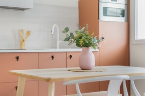 A kitchen with a wooden table, a pink vase with flowers, and a white sink.