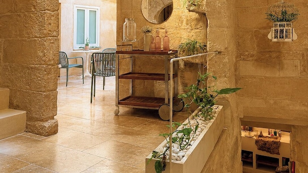 Un interior con paredes de piedra, piso de baldosas, zona de comedor con sillas, una mesa y una lámpara colgante.