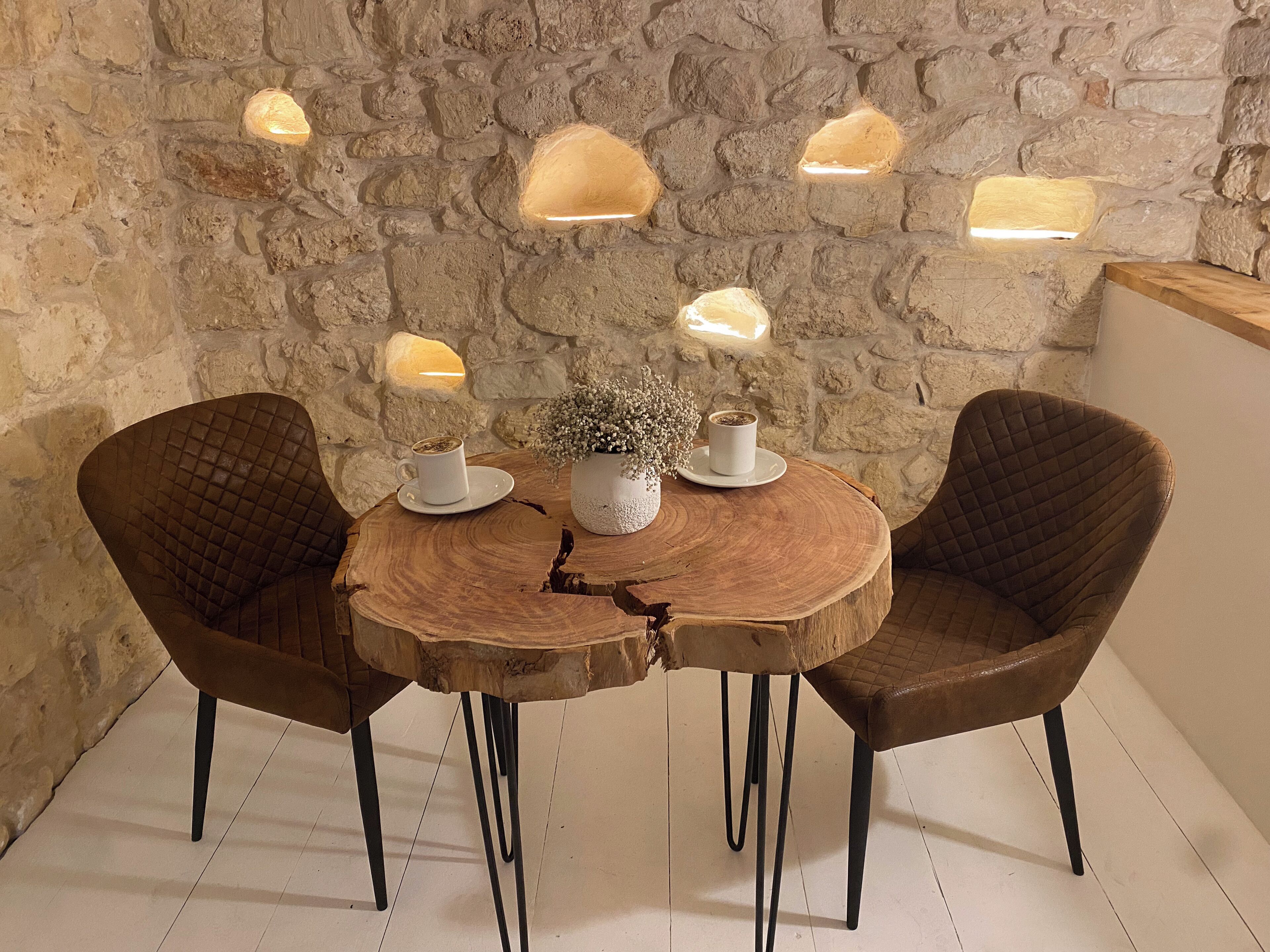 A rustic wooden table with two chairs, a potted plant, and two cups on a stone wall backdrop.