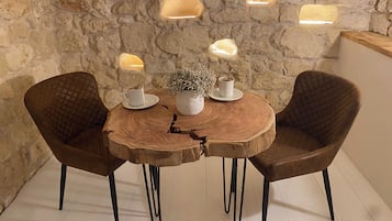 A rustic wooden table with two chairs, a potted plant, and two cups on a stone wall backdrop.