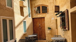 Un patio con paredes de piedra, una puerta de madera y zona de estar exterior con mesas y sillas.