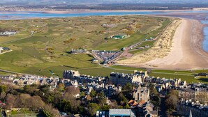 A coastal town with a beach, green fields, and historic buildings.