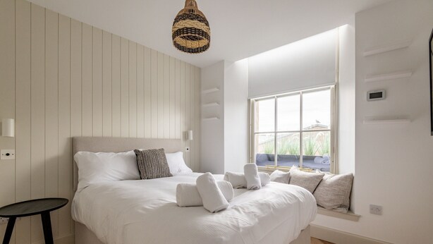 A bedroom with a large bed, a bedside table, a window with a view, and a hanging light fixture.