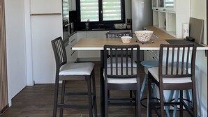 Cozinha moderna com área de refeições, piso de madeira e uma janela grande com persianas.