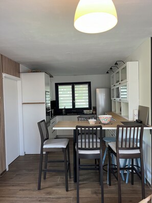 A modern kitchen with a dining area, wooden flooring, and a large window with blinds. - MAISON D'Y (Moliets et Maa)