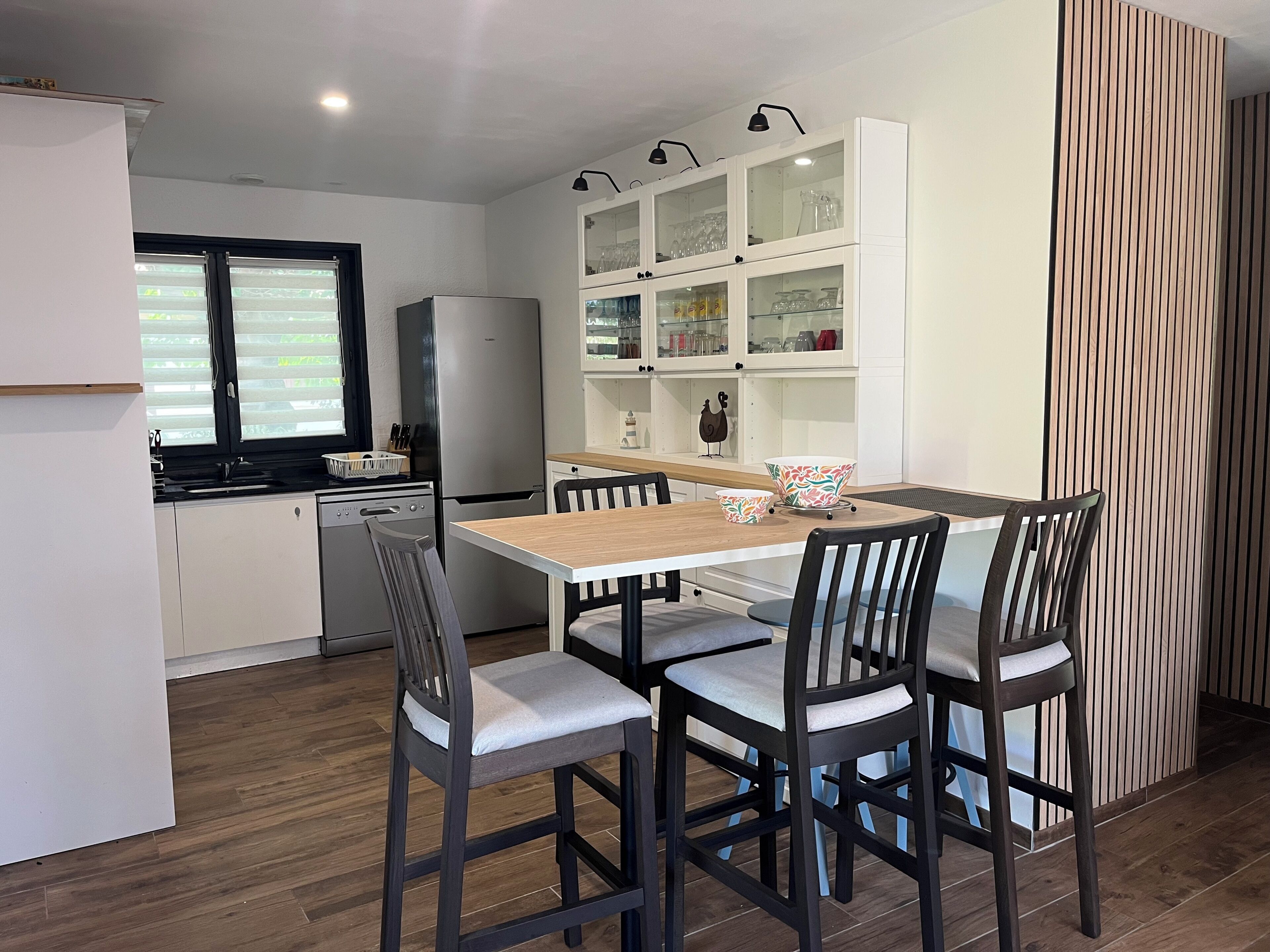 A modern kitchen with a dining area, featuring a wooden table, four chairs, and built-in cabinets with glass doors.