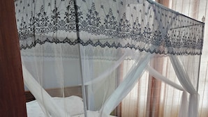 A bed with a canopy, wooden headboard, and a yellow mat. - North Gates - 3 Spacious Ensuite Family Home (Dodoma)