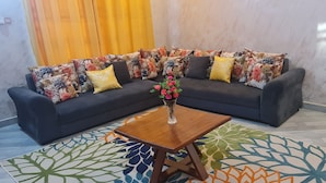 A modern living room with a dark sofa, colorful cushions, a wooden coffee table, and a patterned rug. - North Gates - 3 Spacious Ensuite Family Home (Dodoma)