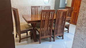 A dining area with a wooden table and chairs, a tiled floor, and a textured wall. - North Gates - 3 Spacious Ensuite Family Home (Dodoma)