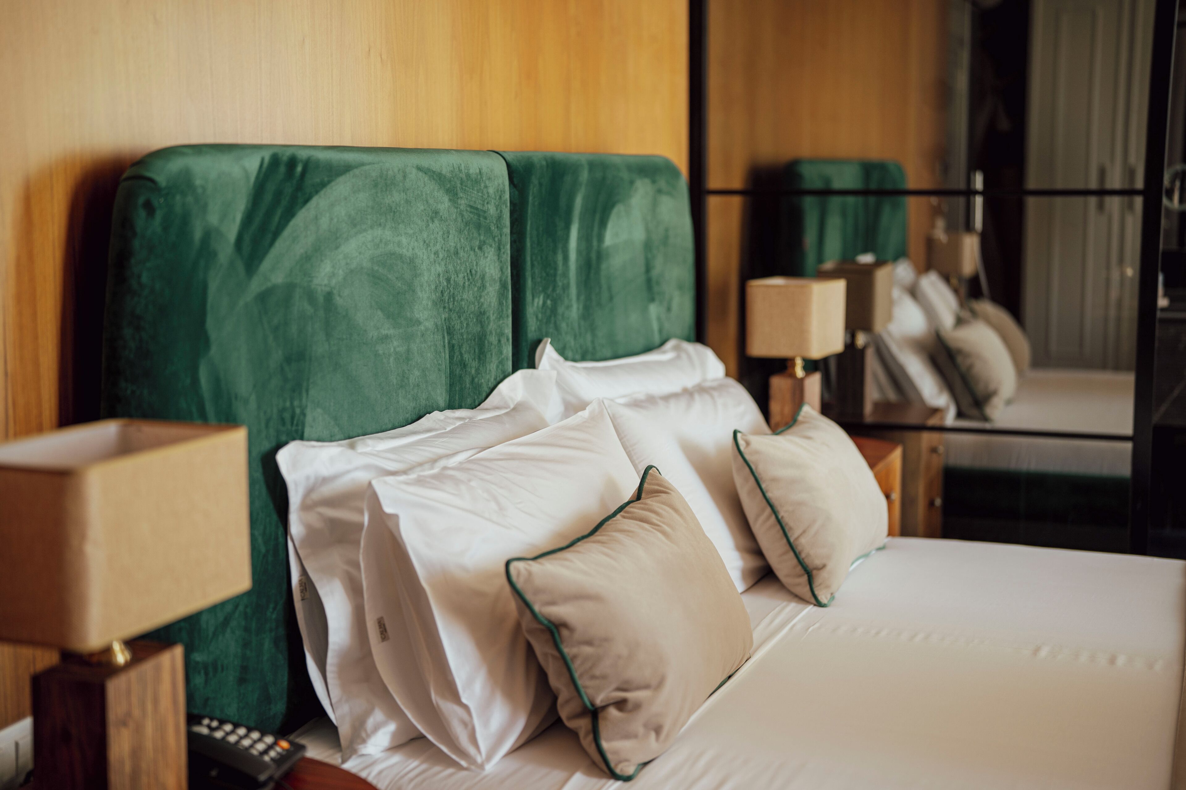 A hotel room with a bed, pillows, a nightstand, a lamp, and a mirror.