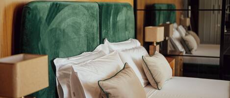 A hotel room with a bed, pillows, a nightstand, a lamp, and a mirror.
