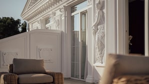 Un bâtiment de style classique, doté de colonnes richement décorées et d’une statue, de meubles en osier et d’une porte en verre.