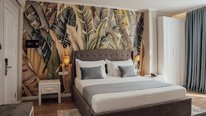 Une chambre à coucher avec un grand lit, une table de chevet, une armoire et un mur orné d’un motif de feuilles.