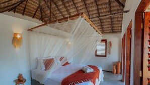 A room with a bed under a thatched roof, a small stool, and a wall-mounted light fixture. - Vila Ronquinha (Tutóia)