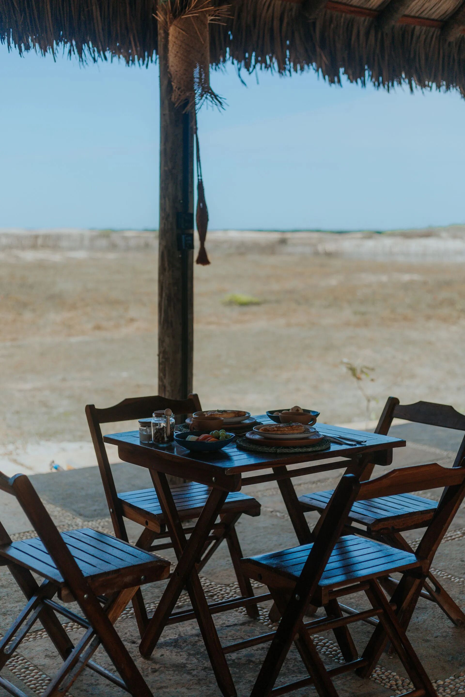 A table set outdoors with chairs, a thatched roof, and a view of the beach.