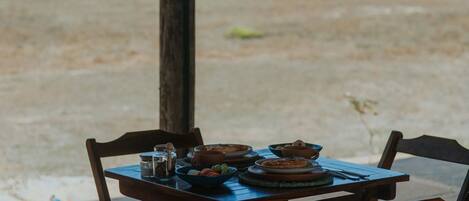 A table set outdoors with chairs, a thatched roof, and a view of the beach.