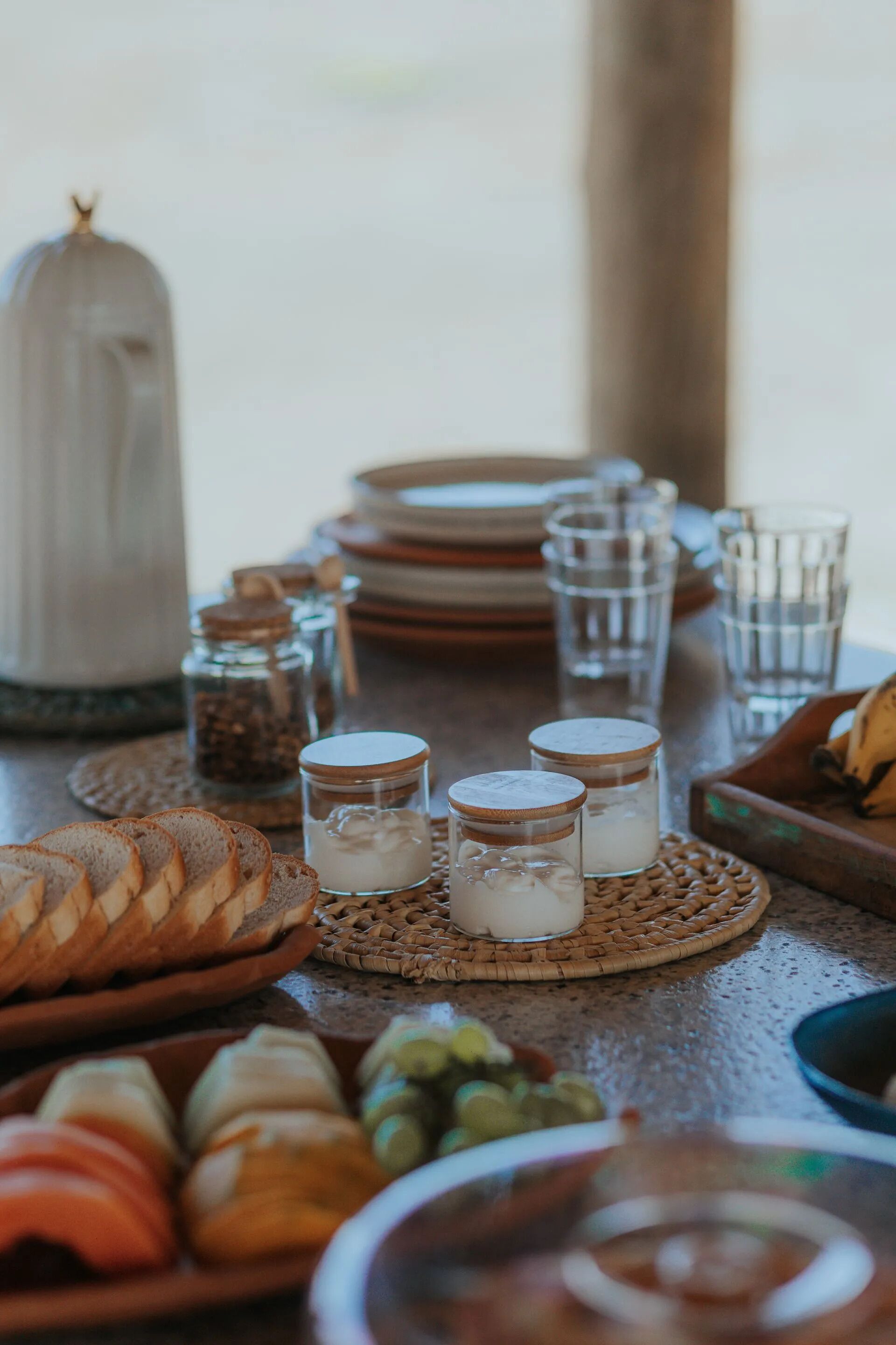 Une table à manger avec du pain, du fromage et des pots de condiments.