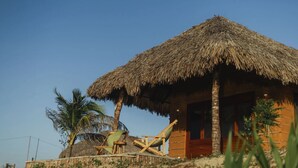A thatched-roof hut with a wooden door, a small porch, and a pair of wooden chairs. - Vila Ronquinha (Tutóia)