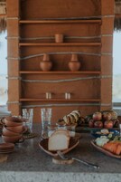 Una cocina rústica con macetas de terracota, vasos, pan y frutas sobre la encimera.