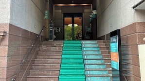A staircase leading to a hotel entrance with a green carpet and signs indicating multiple hotel rooms.