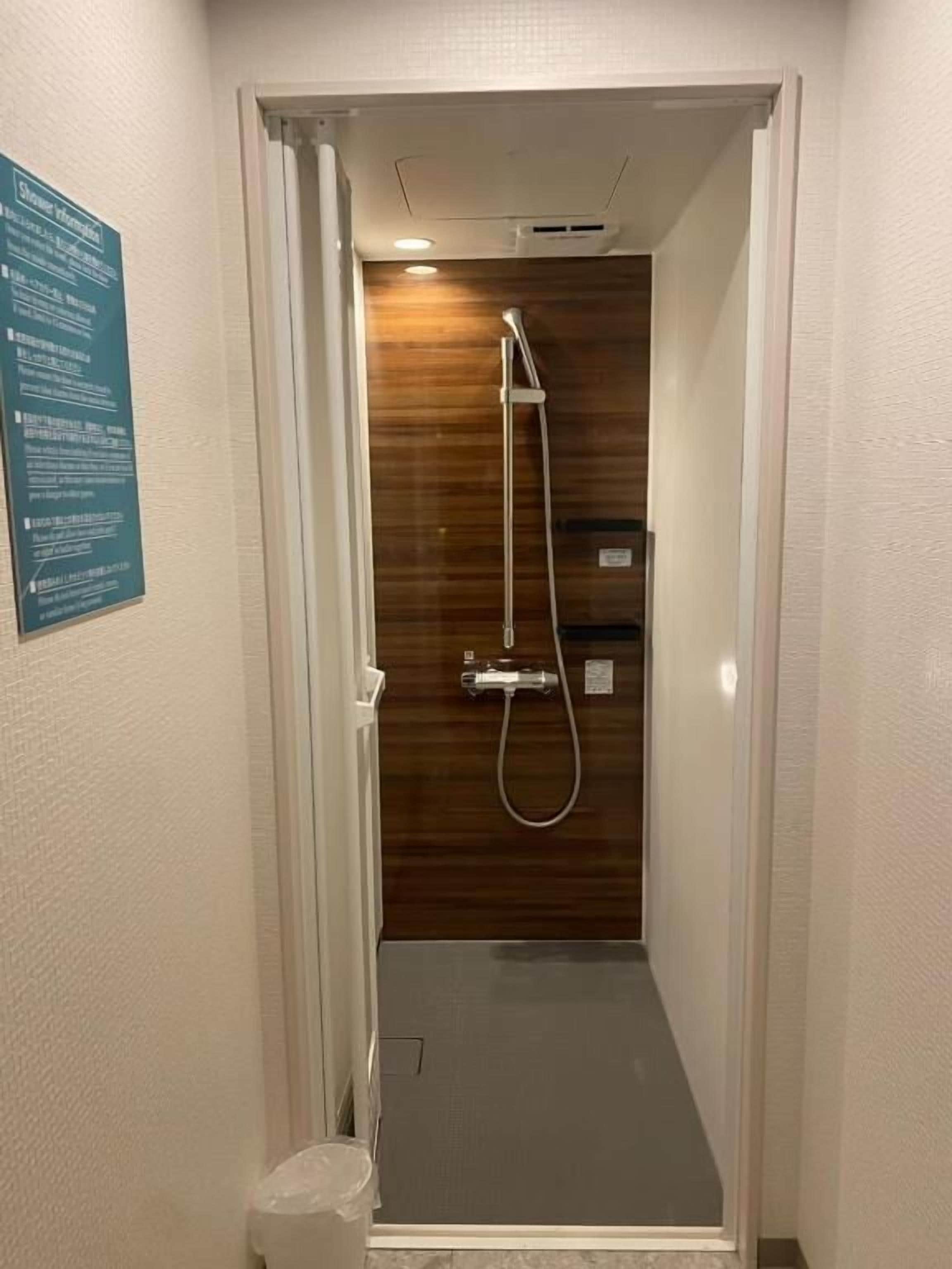 Un couloir étroit mène à un espace douche, avec un mur en bois et un panneau indicateur sur la gauche.