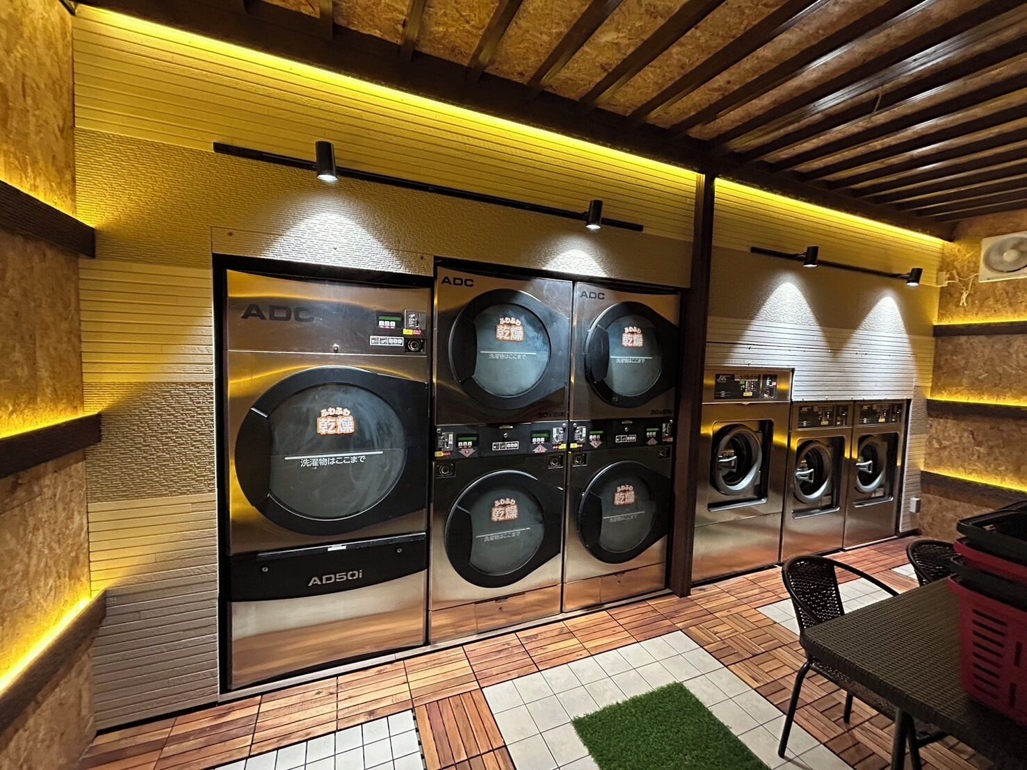 A laundry facility with multiple washing machines, a tiled floor, and wooden beams on the ceiling.
