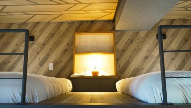 A room with two bunk beds, a wooden ceiling, a window with a lamp, and a small table.