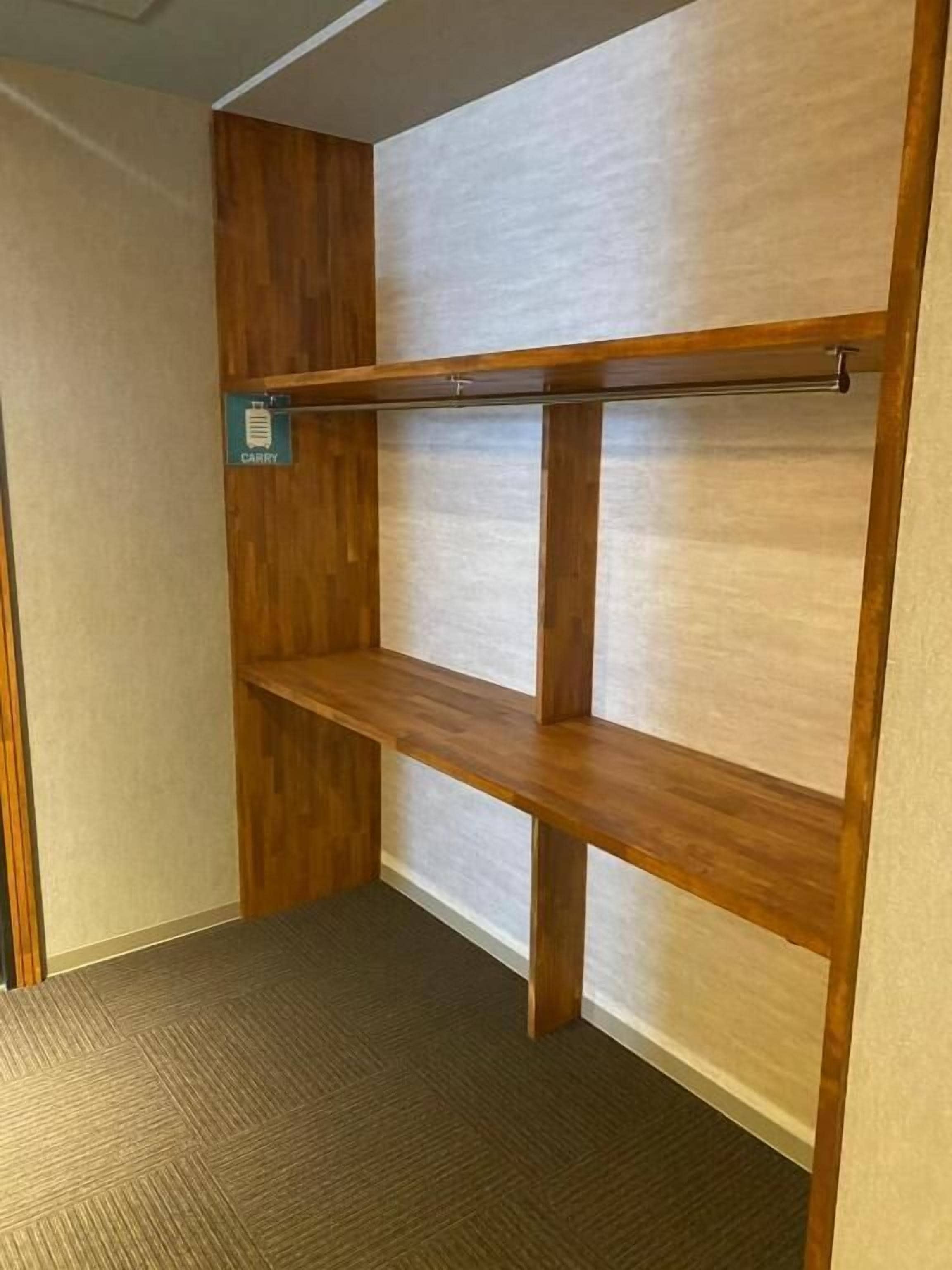 Un rincón de una habitación con una estantería de madera adosada a la pared, suelo de madera y alfombra.