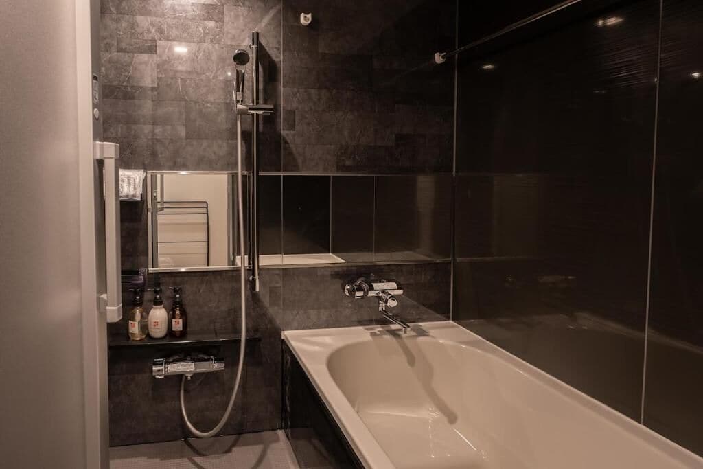Uma casa de banho moderna com banheira, chuveiro, área de duche com parede de vidro e lavatório com espelho e prateleiras.