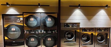 A laundry facility with multiple washing machines and dryers, wooden ceiling beams, and a tiled floor.