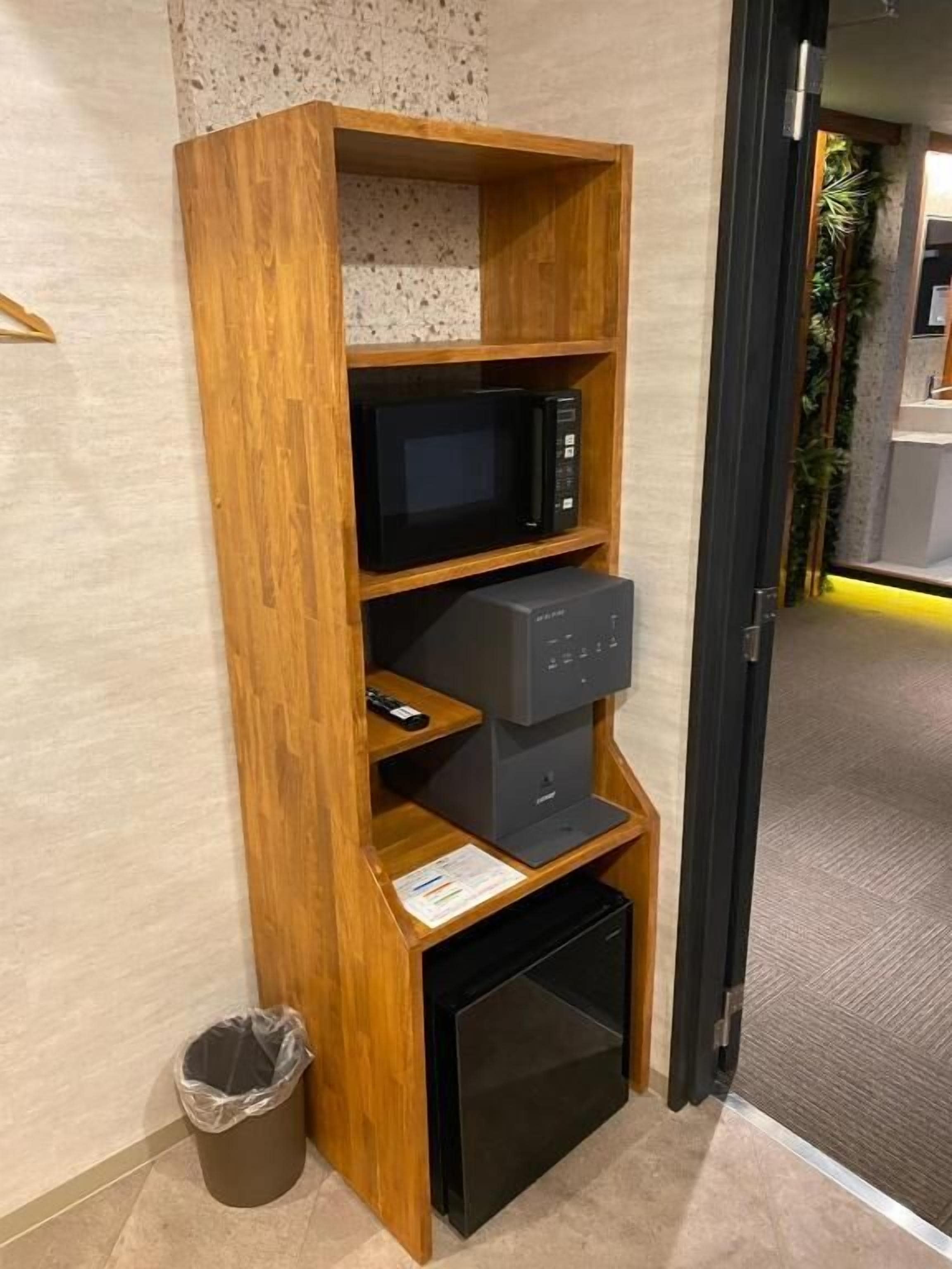Ein Holzbodenregal mit einer Mikrowelle, einem kleinen Kühlschrank und einem Mülleimer.