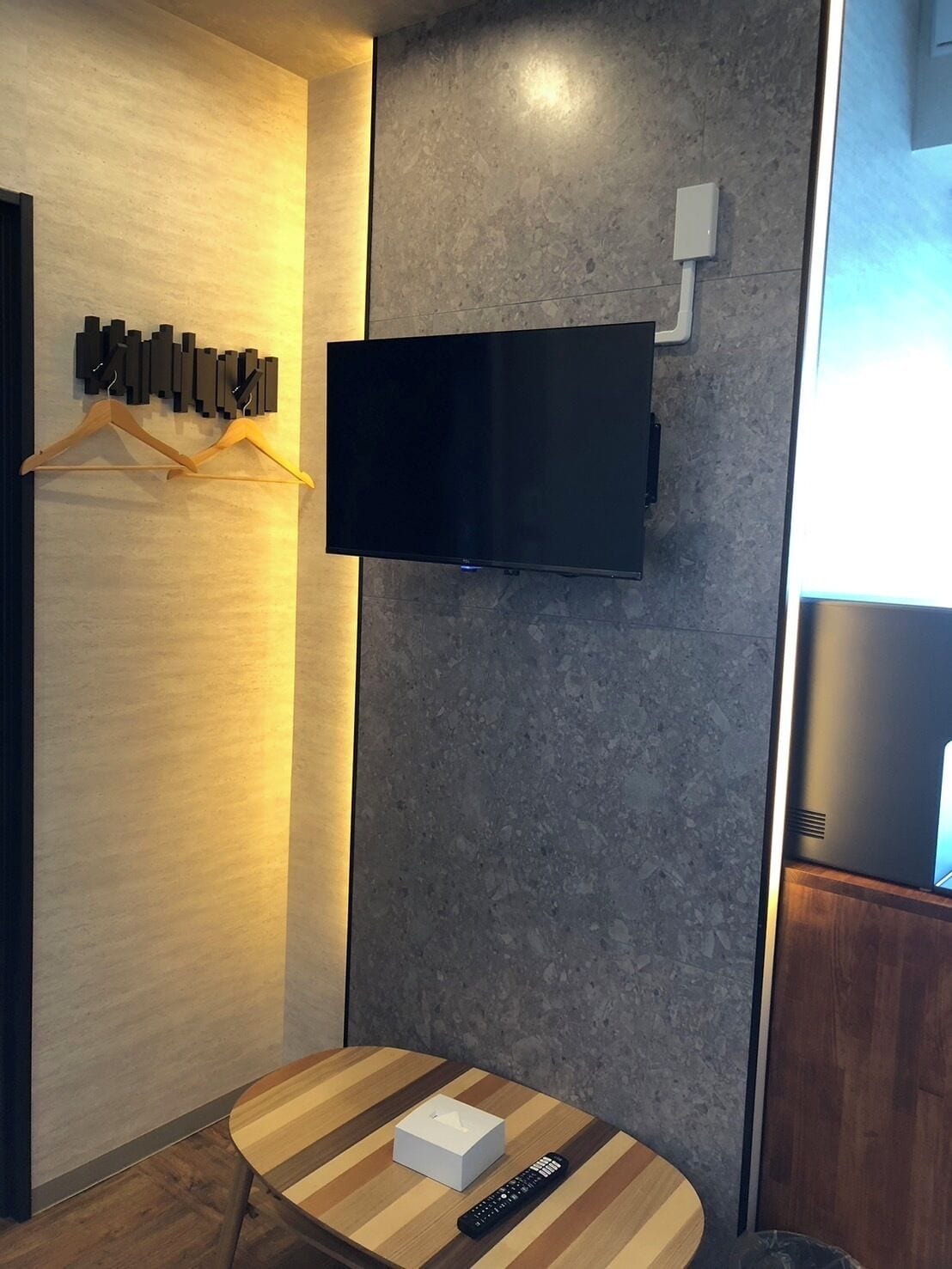 A modern room with a flat-screen TV mounted on a textured wall, a wooden table with a remote control, and a white box.