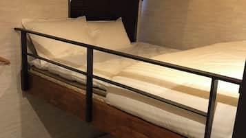 Una litera con estructura de madera y ropa de cama blanca, una ventana pequeña con persianas y una pared de piedra.