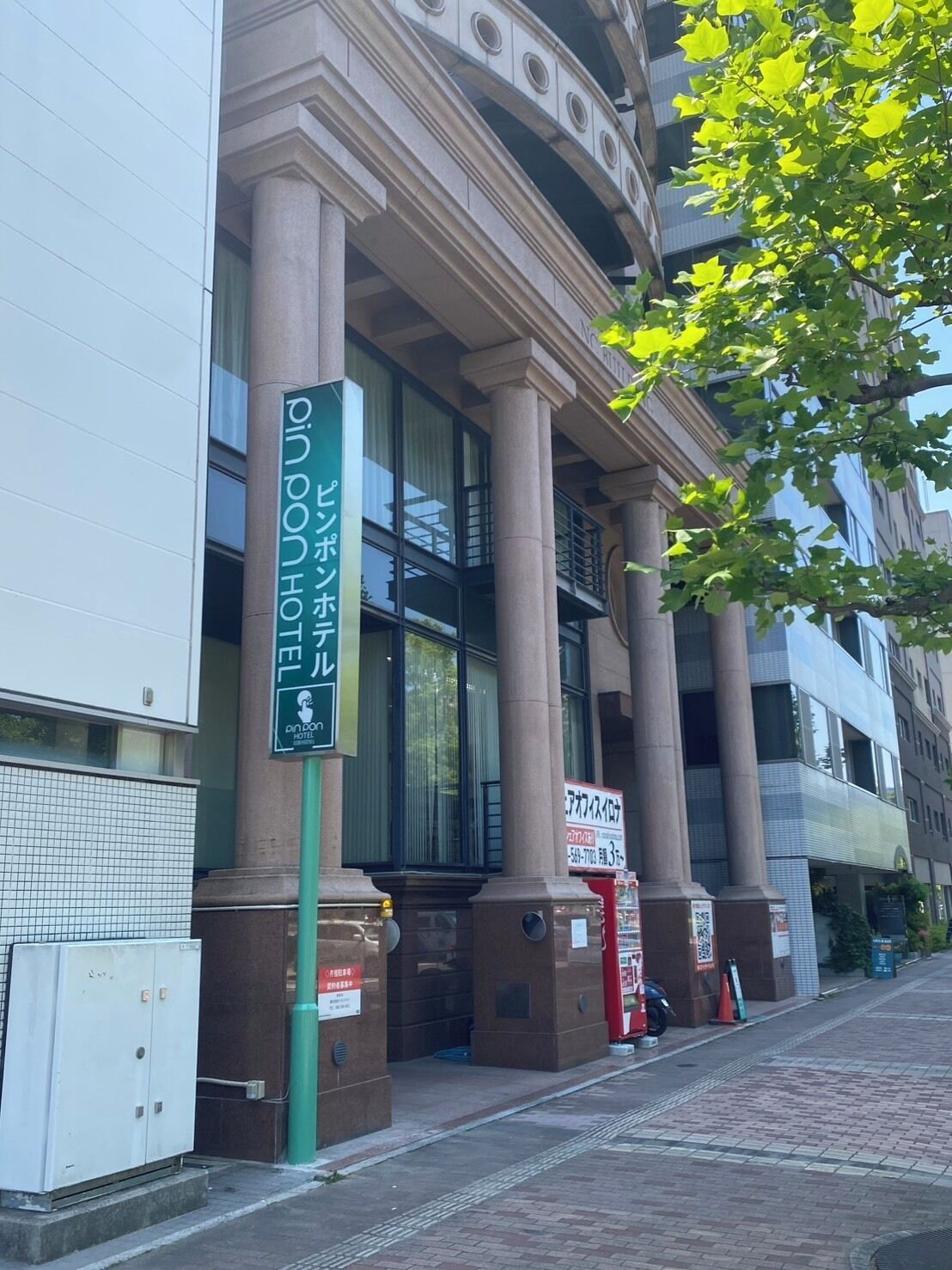 A building with large columns, a sign for a hotel, and a tree with green leaves.