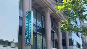 A building with large columns, a sign for a hotel, and a tree with green leaves.