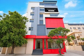 A multi-story building with a prominent red and grey facade, a sign indicating it is serviced by OYO, and a staircase leading to the entrance.