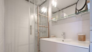 A modern bathroom with a glass shower enclosure, a white vanity with a mirror, and a wooden stool. - House with a garden and a nearby beach (Agde)