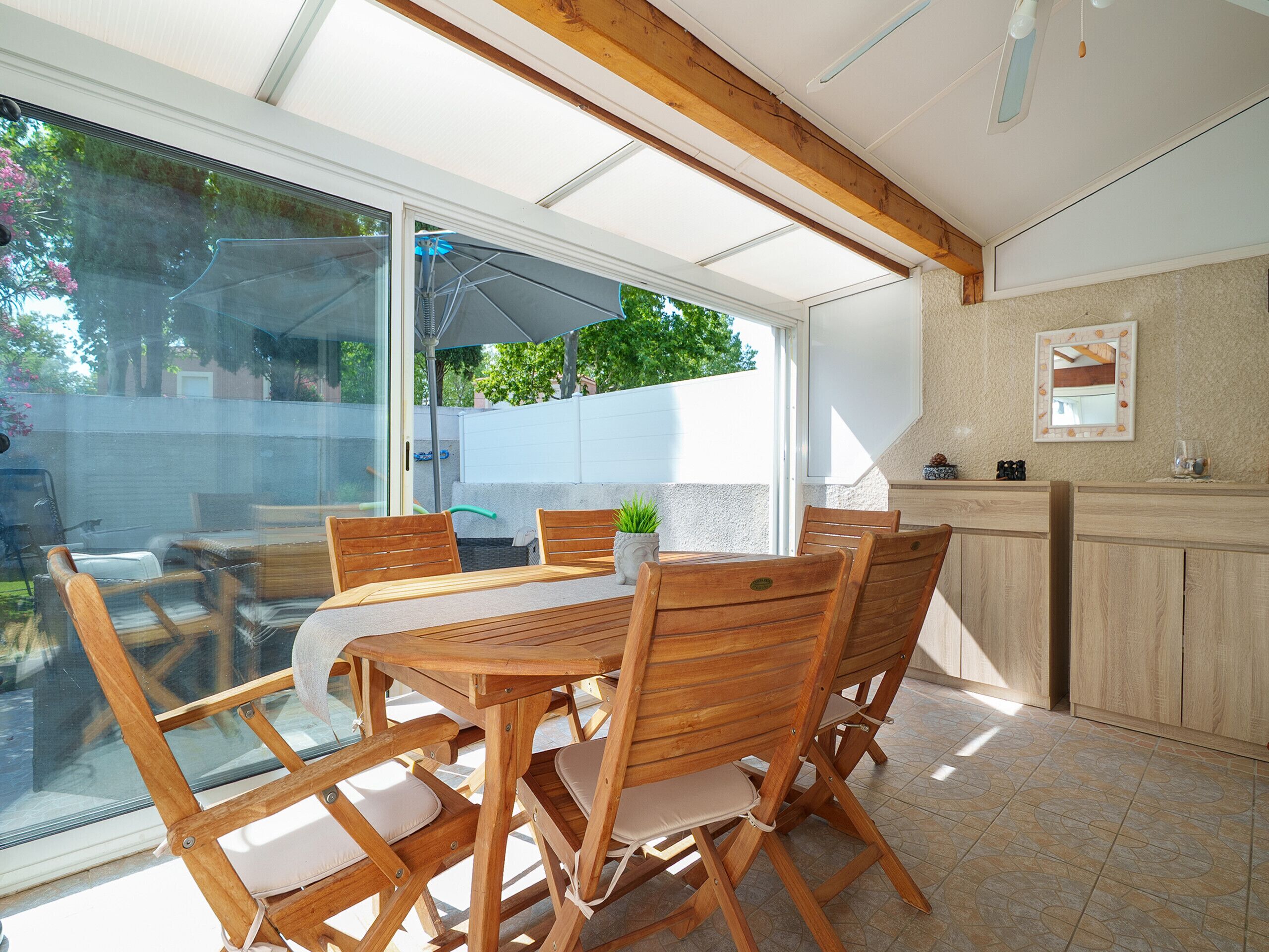 Une cuisine et une salle à manger à aire ouverte, avec des meubles en bois, une porte vitrée donnant sur l’extérieur et une petite plante en pot posée sur la table.