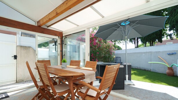 A covered patio with a table and chairs, a grill, and a large umbrella. - House with a garden and a nearby beach (Agde)