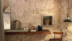 Une pièce aux murs de pierre, avec un comptoir en bois, une chaise, un miroir, une plante en pot et un luminaire suspendu.