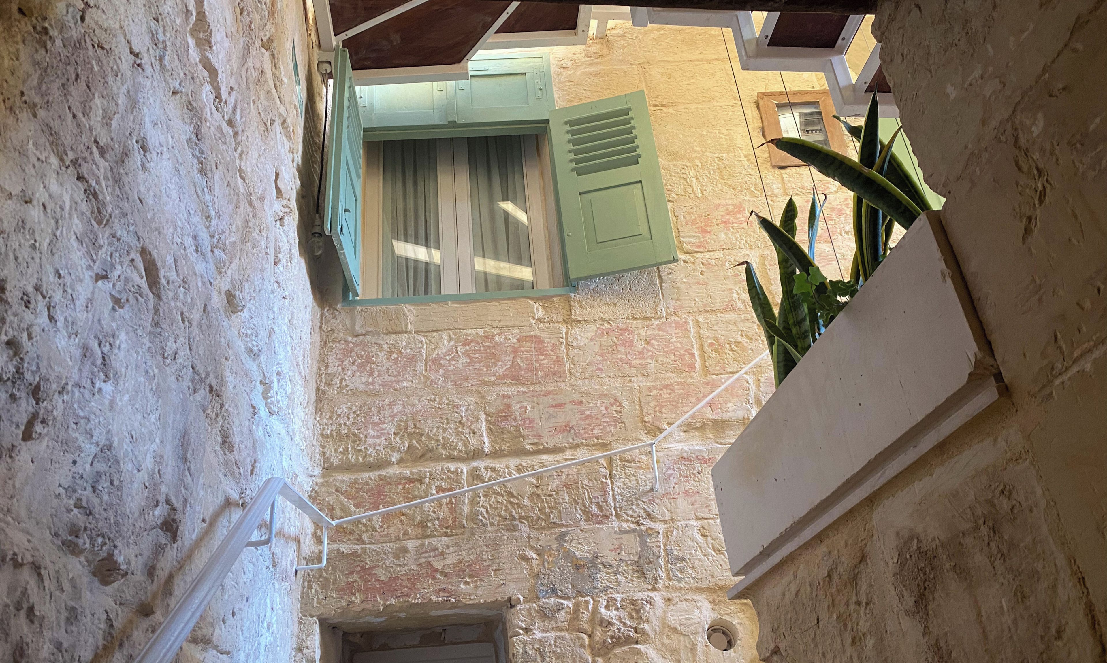 A narrow corridor with stone walls, a wooden door, and a window with shutters.