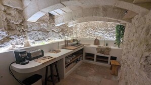 Une cuisine rustique aux murs de pierre, une fenêtre offrant une belle vue, une machine à café et des tabourets en bois.