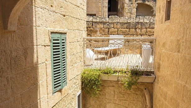Une ruelle étroite bordée d’immeubles en pierre, avec une porte en bois et un balcon doté d’un garde-corps en fer forgé.