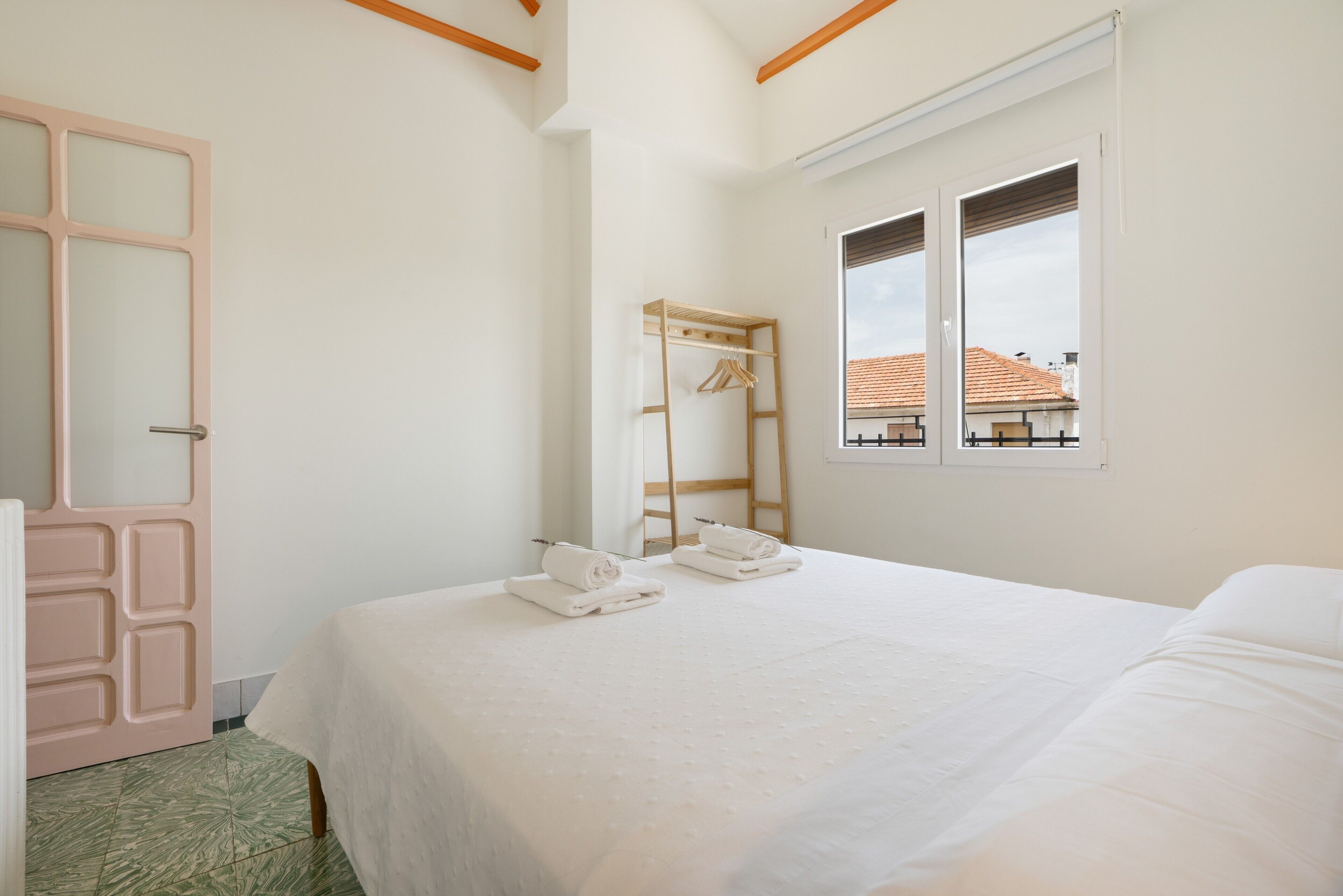 Un dormitorio con una cama, un tendedero de madera, un espejo y una ventana con vistas a edificios.