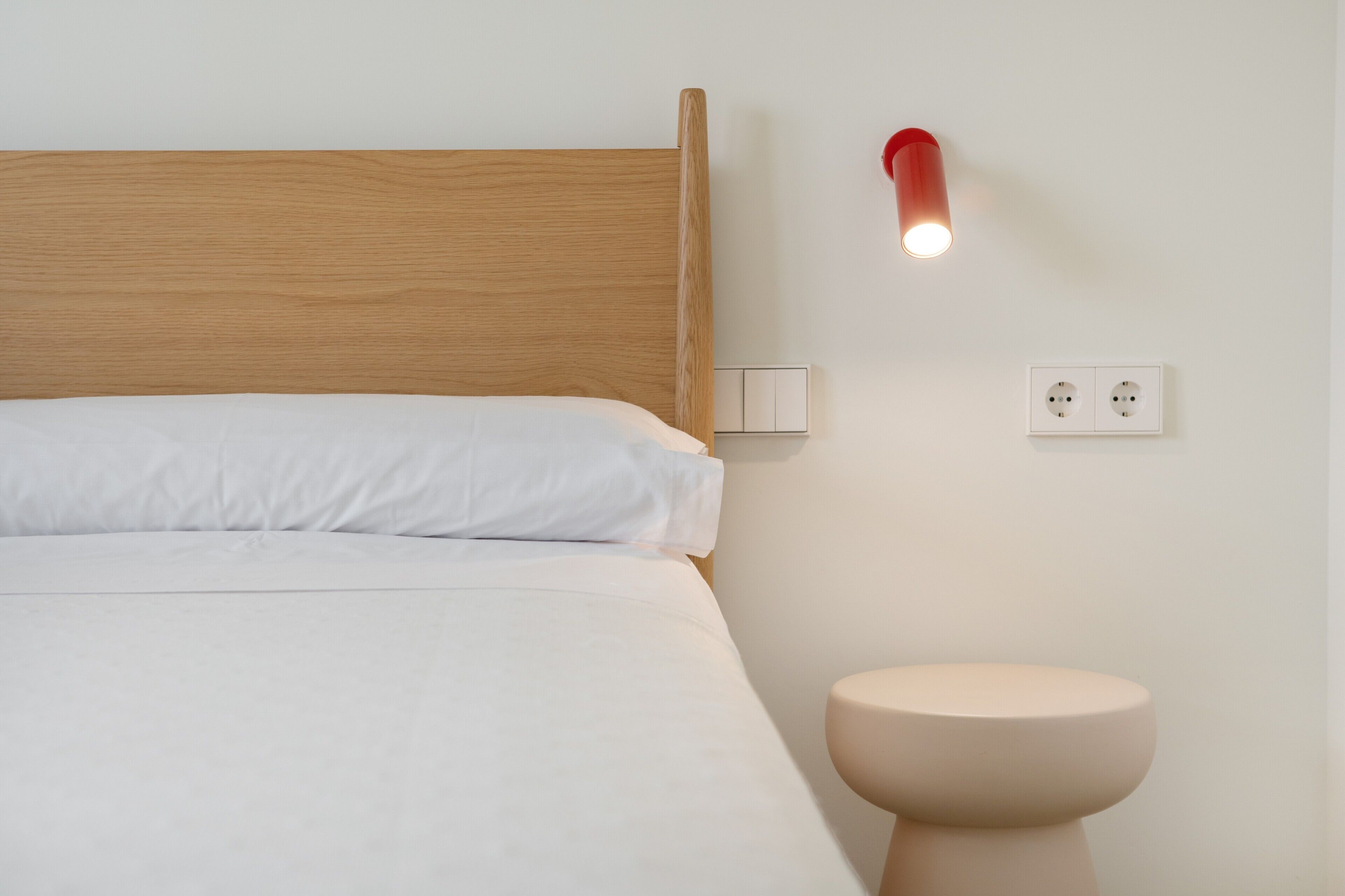 En seng med træsenggavl, et natbord, en vægmonteret lampe og en stikkontakt.