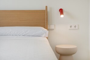 A bed with a wooden headboard, a bedside table, a wall-mounted light, and a wall socket.