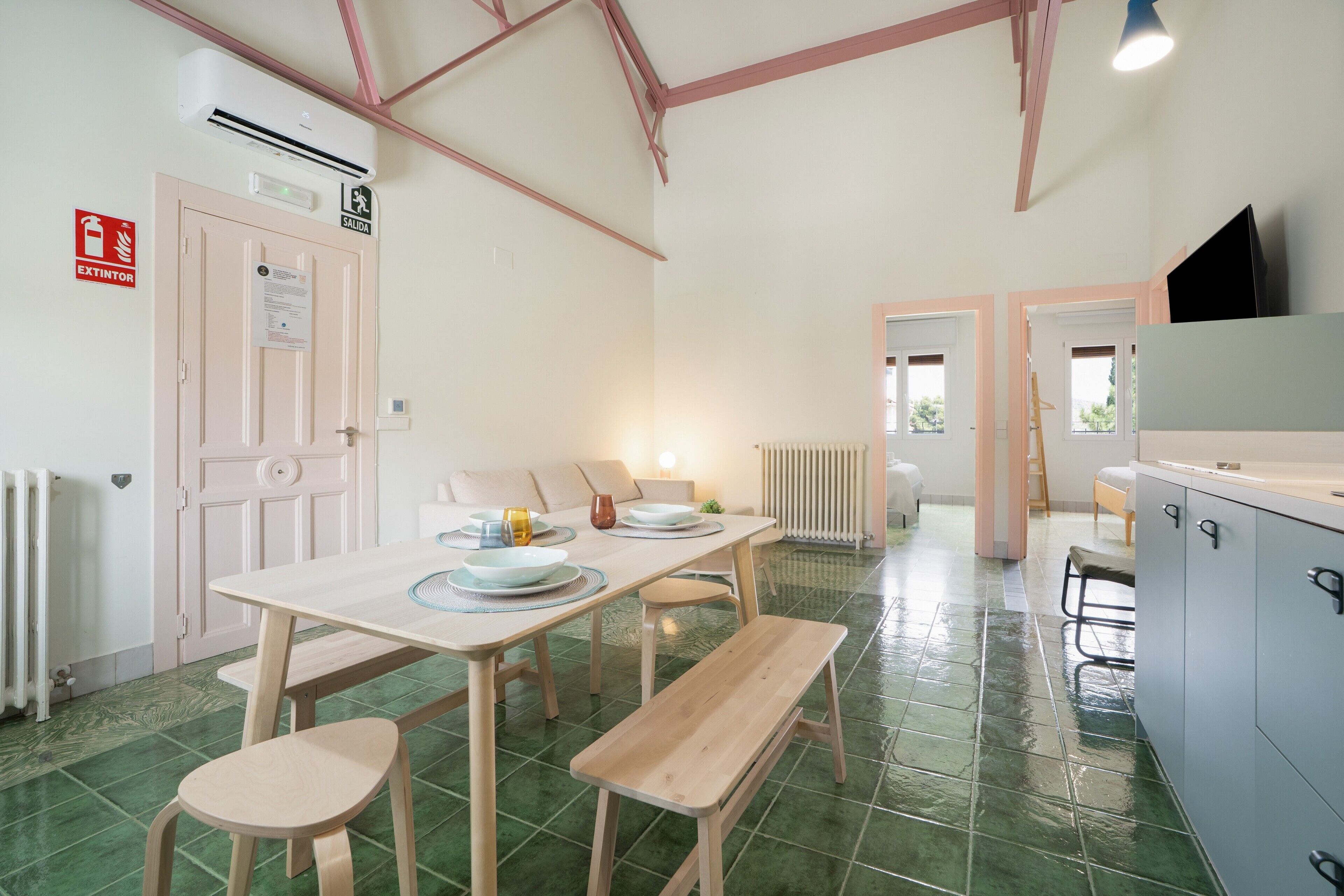 A room with a table, chairs, a bench, a radiator, an air conditioning unit, and a television.
